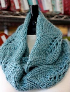 a blue knitted scarf sitting on top of a white cup in front of a shelf