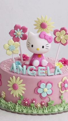 a hello kitty birthday cake with flowers and an angel topper on it's side