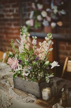 a wooden box filled with lots of flowers on top of a table next to candles