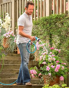 a man is using a hose to water the flowers in his garden steps while watering them