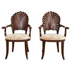 a pair of wooden chairs with shell backrests and upholstered seat cushions