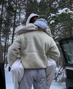 a man is standing in the snow with his back turned to the camera, wearing a white coat and grey pants