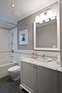 a bathroom with gray and white walls, tile flooring and a large mirror above the sink