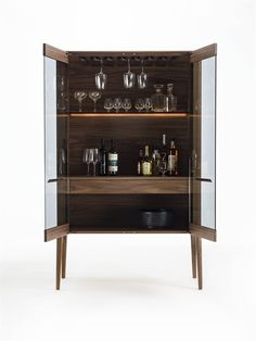 an open cabinet with wine glasses and liquor bottles on the bottom shelf, in front of a white background