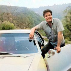 a man sitting on the hood of a car with his hand on the door handle