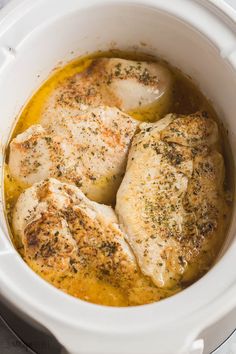 three pieces of chicken in a white crock pot with broth and seasoning