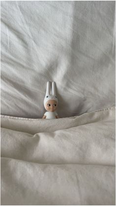 a small stuffed animal sitting on top of a white bed sheet covered in linens