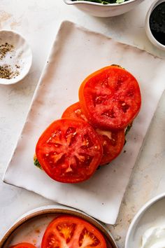 sliced tomatoes on a cutting board next to bowls of yogurt