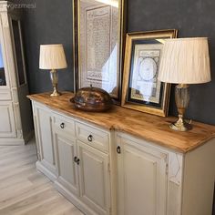 two lamps are sitting on top of a white cabinet with gold accents and framed pictures