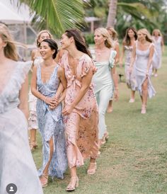 a group of women walking down a grass covered field next to each other in dresses