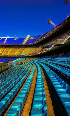 rows of empty seats in an empty stadium with bright lights on the stands and blue sky above