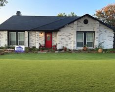 a white brick house with a red front door and green grass in front of it