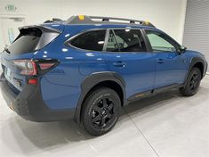 the back end of a blue car in a garage with white walls and grey flooring