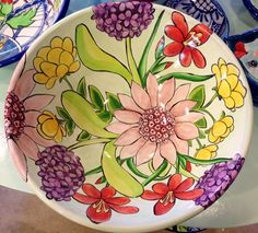 a bowl with flowers painted on it sitting next to other plates and bowls in the background