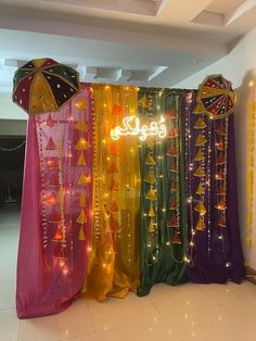 an array of colorful drapes with lights on them in front of a white wall