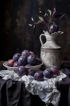 a still life with plums and a pitcher on a table cloth next to it