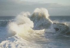 a large wave crashing into the ocean on a cloudy day