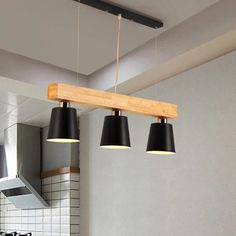 three lights hanging from a wooden beam in a kitchen with black and white tiles on the walls