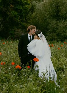 a bride and groom kissing in a field full of poppies with trees in the background