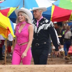 a man and woman in cowboy hats walking through an open area with tents behind them