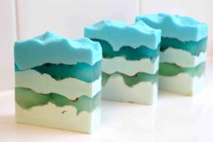 three pieces of soap sitting on top of a white counter covered in blue and green liquid