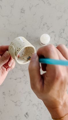 someone is holding a cup in their left hand and writing on it with a blue pen