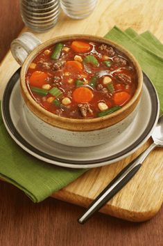 a bowl of chili soup on a plate with a spoon and napkin next to it