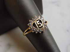 A WOMENS VINTAGE ESTATE 14K GOLD, LA QUINCEANERA HEART RING. THE RING IS A SIZE 6.75 AND WEIGHS 2.4g. THE STONES ARE EITHER CUBIC ZIRCONIA OR CRYSTALS. THIS IS A LOVELY GIFT FOR A YOUNG WOMAN TURNING 15 YEARS OF AGE. ANY QUESTIONS PLEASE DONT HESITATE TO ASK. BE SURE TO CHECK OUT SOME OF MY OTHER GREAT ITEMS UP FOR SALE. THANK YOU Oval Ring With Hallmark For Anniversary, Round Engraved Ring With Hallmark For Anniversary, Vintage Gold Cluster Ring For Anniversary, Vintage Anniversary Rings With Hallmarks, Vintage Anniversary Ring With Hallmarks, Vintage Hallmarked Ring For Anniversary, Antique Gold Cluster Ring For Anniversary, Heirloom Engraved Ring With Hallmark For Anniversary, Gold Engraved Ring With Center Stone For Anniversary