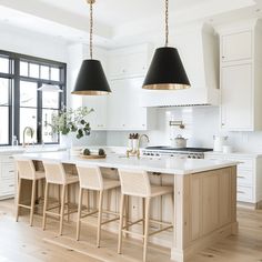 a large kitchen with white cabinets and black lamps hanging from the ceiling over the island