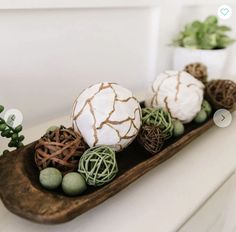 three decorative balls on a wooden tray with plants in the backgroung and white vases behind them