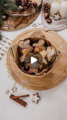 a wooden bowl filled with cookies on top of a table next to candles and pine cones