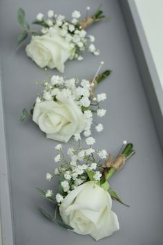 three white roses and baby's breath are arranged in a row on a gray surface