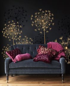 a couch with some pillows on it in front of a wall decorated with dandelions