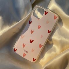 an iphone case with hearts on it laying on a satin surface, next to a white sheet