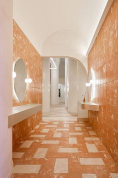 an orange and white tiled hallway leading to two sinks in the center with mirrors on either side