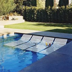 an empty swimming pool with sun loungers in the foreground and grass behind it