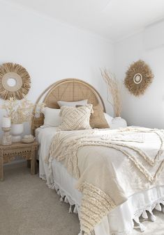 a white bedroom with wicker headboard and round mirrors on the wall above the bed