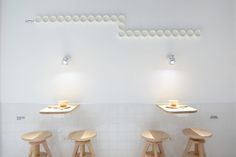 three wooden stools sit in front of a white wall with round lights above them