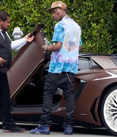 two men standing in front of a brown sports car