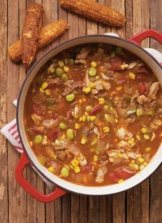 a pot filled with chicken and corn soup next to some crackers on a wooden table