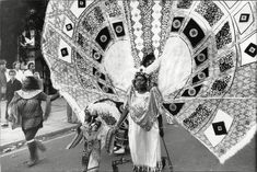 an old photo of a woman in costume holding up a large kite on the street