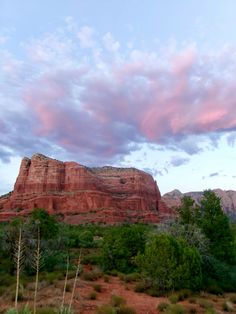 the mountains are covered in red rocks and green trees under a blue sky with pink clouds