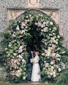 a bride and groom standing in front of a floral arch