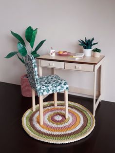 a desk with a chair, potted plant and rug on the floor in front of it