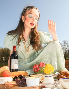 a woman sitting at a table with food and wine in front of her, making the peace sign