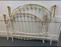 a white iron bed frame with gold posts and headboard, against a white wall