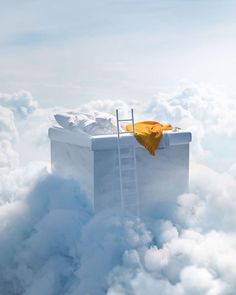 a ladder leading up to an open box in the clouds with a yellow cloth on it