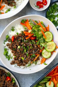 two plates with rice, carrots and meat on them next to cucumbers