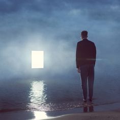 a man standing in the water looking out at an open door that is partially obscured by fog