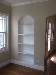 an empty room with a white bookcase in the corner and a window on the far wall